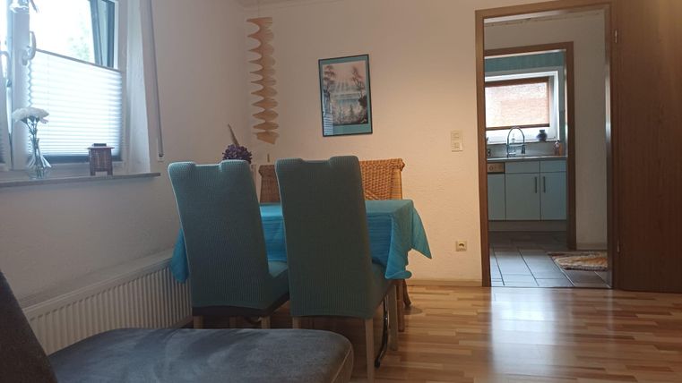 A cozy dining area with a table and chairs. In the background, the kitchen is visible.