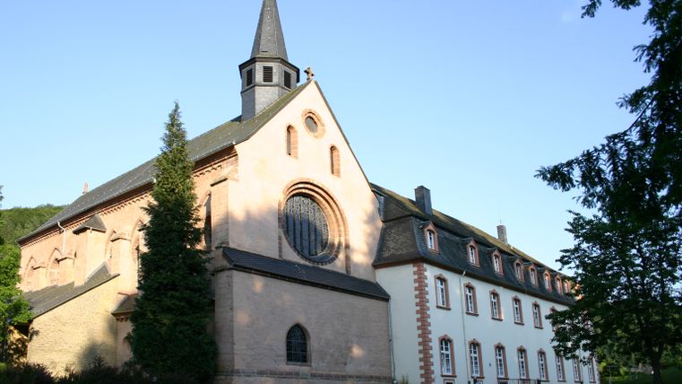 Kloster St. Thomas mit gotischer Architektur und Rosettenfenster, umgeben von Bäumen.