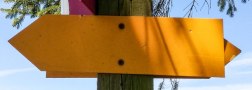 A yellow signpost on a wooden post, surrounded by branches and blue sky., © TI Bitburger Land