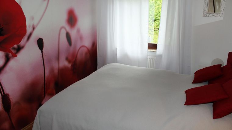 Une chambre confortable avec un grand lit et des coussins rouges. Sur le mur, il y a un motif décoratif de coquelicots rouges.