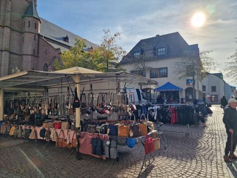A lively market stall with colorful bags and handmade textiles. The stalls are set up under red tents and offer a variety of products.