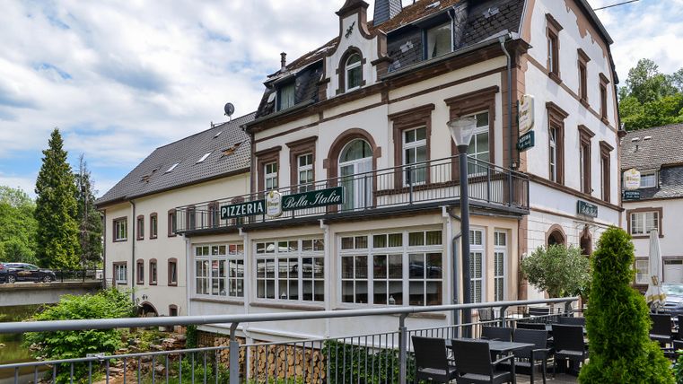 Ein charmantes Gebäude, das eine Pizzeria beherbergt. Draußen sind Sitzgelegenheiten und eine schöne Aussicht auf die Umgebung.