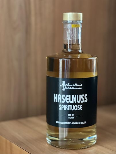 Eine Flasche Haselnuss-Spirituose steht auf einem Holztisch. Die Flasche hat ein schlichtes Etikett mit der Aufschrift „Haselnuss Spirituose“.