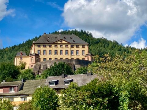 Ein beeindruckendes Schloss auf einem Hügel, umgeben von grünen Bäumen. Der Himmel ist blau mit weißen Wolken.