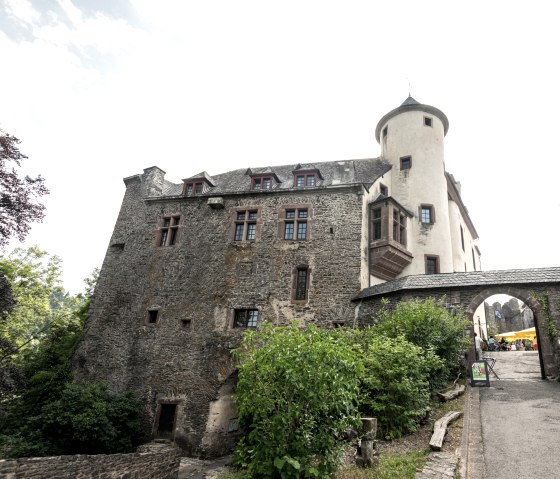 Burg Neuerburg mit steinernen Mauern und einem Turm. Ein Torbogen führt zu einem Innenhof. Umgeben von Bäumen und Pflanzen., © Eifel Tourismus GmbH, D. Ketz