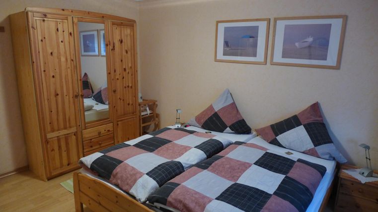 A cozy bedroom with a double bed and checkered bedspreads. Two pictures hang on the wall, and there is a wooden wardrobe with a mirror.