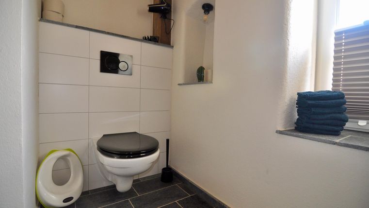 A modern bathroom with a toilet and gray tiles. Towels are neatly stacked, and there is a small window nook.