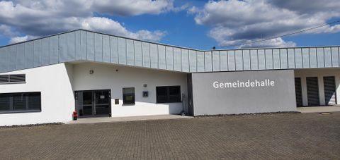Ein modernes Gemeindezentrum mit einem klaren, einladenden Design. Der Himmel ist blau mit einigen weißen Wolken.