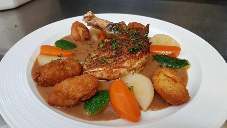 Ein köstliches Gericht mit gebratenem Hähnchen, umgeben von buntem Gemüse und köstlichen Kartoffeln. Die Speise ist ansprechend angerichtet und sieht sehr einladend aus.