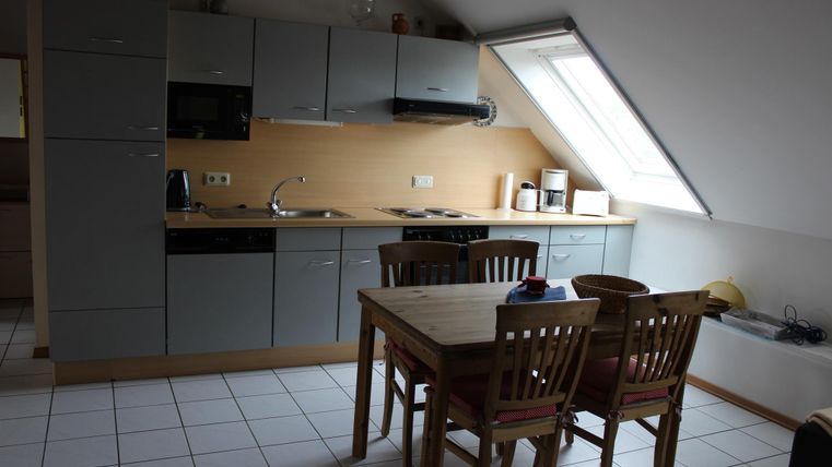 Eine moderne Küche mit grauen Schränken und einem Essbereich aus Holz. Das Zimmer hat ein Fenster, das viel Licht hereinlässt.