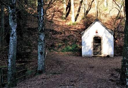 White chapel in the forest, surrounded by trees and autumn leaves. The entrance is made of wood, the surroundings are quiet and secluded., © TI Bitburger Land