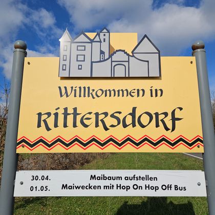 Ein Willkommensschild für Ritterdorf mit einer bunten Gestaltung. Es enthält Informationen zu bevorstehenden Veranstaltungen am 30.04. und 01.05.