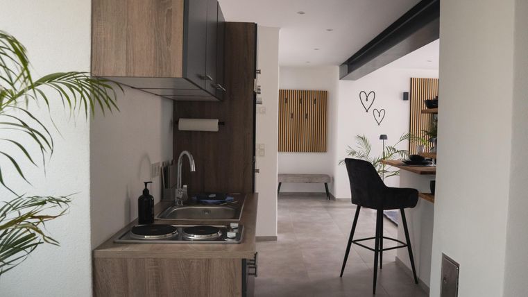 Eine moderne Küche mit Holzmöbeln und einer kleinen Kochstelle. Der Raum ist hell und modern eingerichtet mit Pflanzen und einer gemütlichen Sitzecke.
