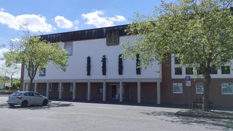 A modern building with a tasteful facade and green trees nearby. There is a parking lot in the foreground.