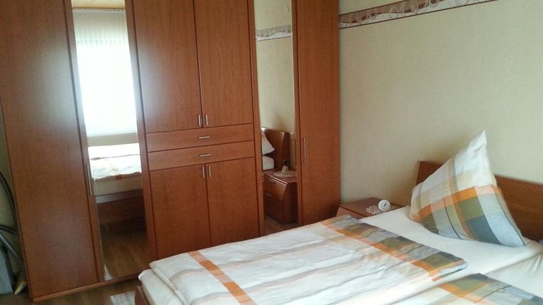 Ein einfaches Schlafzimmer mit einem Doppelbett und einem großen Kleiderschrank. Das Zimmer hat helle Wände und viel Tageslicht.