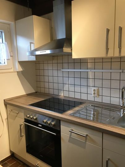 Eine moderne Küche mit hellen Schränken und einer klaren, gefliesten Wand. Der Herd und die Spüle sind funktional integriert.