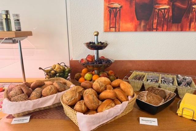 Ein Buffet mit verschiedenen Brotsorten in Körben. Obst in einer Schüssel und Besteck auf einem Tablett sind ebenfalls sichtbar.