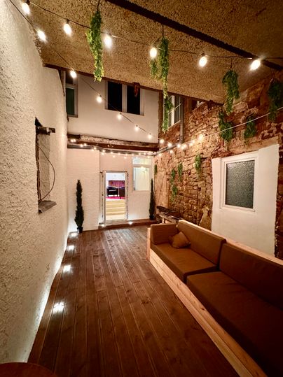 A cozy courtyard with wooden flooring and a comfortable bench. Subtle lights and plants create an inviting atmosphere.