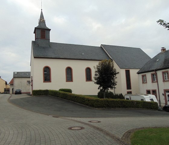 The church of St. Urban in Gindorf with a pointed tower, surrounded by houses and a cobbled path., © Conny Meier