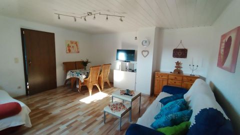 Ein modernes Wohnzimmer mit Holzfußboden, gemütlichen Sofas und einem Esstisch. Es gibt einen Fernseher und dekorative Elemente an den Wänden.