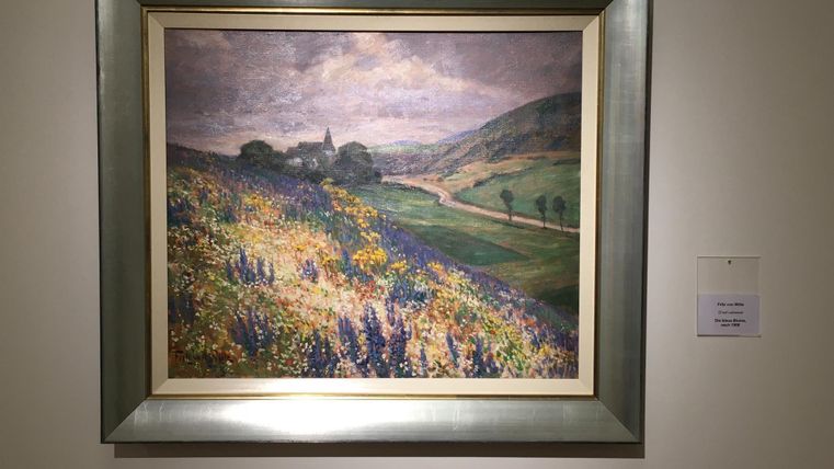 Ein Impressionistisches Gemälde von einer Landschaft mit sanften Hügeln und blühenden Wiesen. Im Hintergrund sind Bäume und ein schmaler Weg zu sehen.