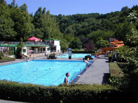 A beautiful swimming area with two pools and a slide. The surroundings are green and inviting.