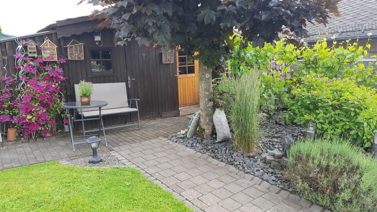 Ein schöner Garten mit bunten Pflanzen und einem kleinen Holzhaus. Auf dem Weg stehen ein Tisch und Stühle zum Entspannen.