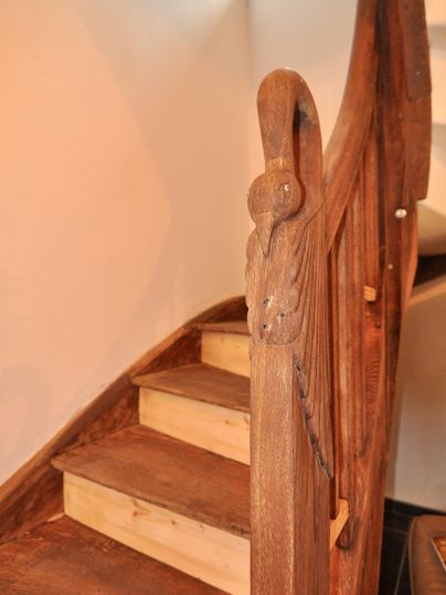 A wooden staircase with an intricately carved handrail. The steps are simple and well-lit.