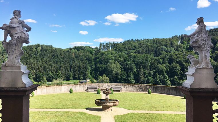 Eine herrliche Aussicht auf einen gepflegten Garten mit Skulpturen und grünen Bäumen im Hintergrund. Der Himmel ist klar und blau, was die Szenerie idyllisch macht.