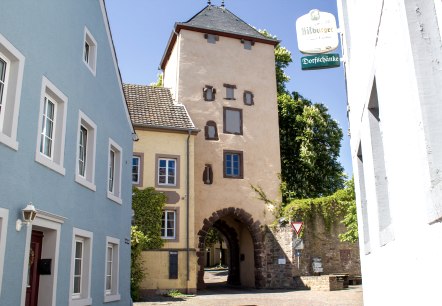 Das Oberes Tor in Dudeldorf, ein historisches Stadttor, umgeben von bunten Häusern und einem Straßenschild. Sonniger Tag mit blauem Himmel., © Tourist-Information Bitburger Land_M. Mayer