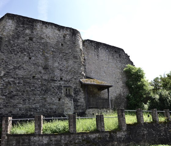 Ruins of Bettingen Castle with massive stone walls, surrounded by green vegetation under a blue sky., © TI Bitburger Land