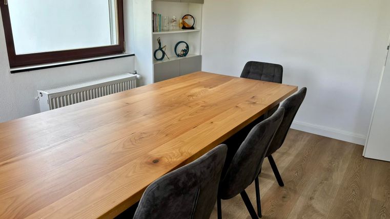 Une salle à manger moderne avec une grande table en bois et des chaises noires. La pièce est lumineuse et au design minimaliste.