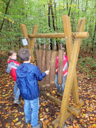 Kinder spielen an einer hölzernen Klangstation im Wald.