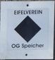 Wanderwegmarkierung des Eifelvereins mit schwarzem Rhombus und Schriftzug 'OG Speicher'.