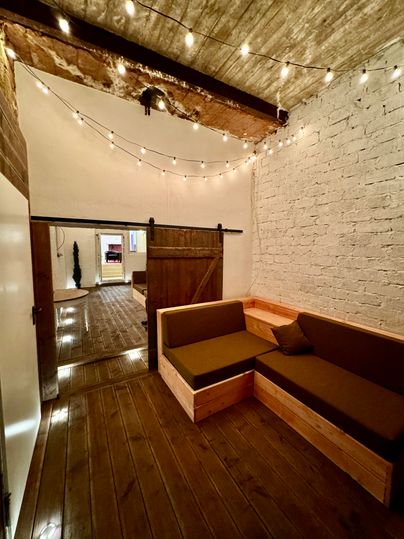 A cozy room with wooden floors and warm lighting. Against one wall are two wooden seating areas with green cushions.