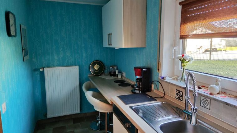 Eine moderne Küche mit hellblauen Wänden und einem unauffälligen Design. Auf der Arbeitsfläche stehen eine Kaffeemaschine und eine kleine Blumenvase.