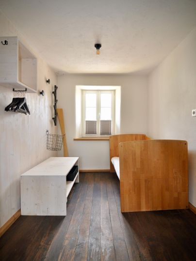 A simple room with a wooden bed and a white table. There is a small desk and a window with a view outside.