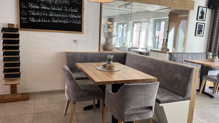 Ein gemütliches Restaurant mit modernen Möbeln und einem Holztisch. An der Wand hängen Tagesgerichte auf einer Tafel.