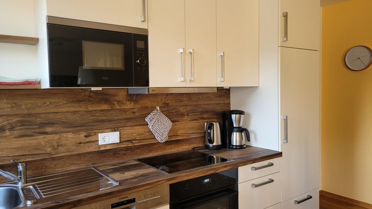 Eine moderne Küche mit Holzregalen und weißen Schränken. Die Ausstattung umfasst einen Herd, eine Mikrowelle und eine Kaffeemaschine.