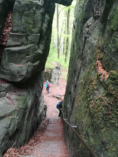 Eine enge Schlucht mit steilen Felsen und Treppen führt hinunter. Im Hintergrund sind Wanderer zu sehen, die den Weg entlanggehen.