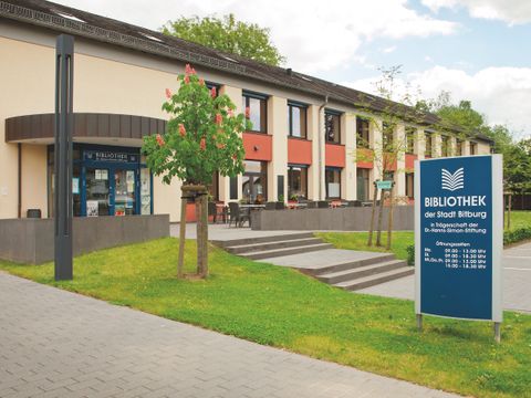 A modern library building with an inviting entrance.
In front of the building, there is a sign with the opening hours.