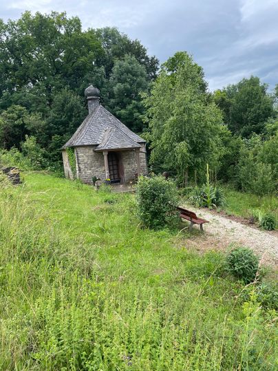 Kleine Steinkapelle inmitten grüner Natur mit Bank und Kiesweg.