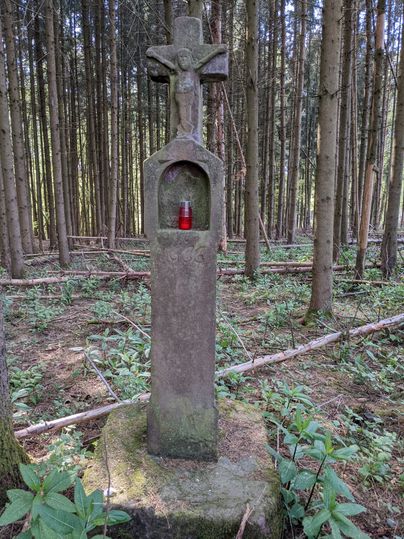 Stone wayside cross with red grave light in the forest.