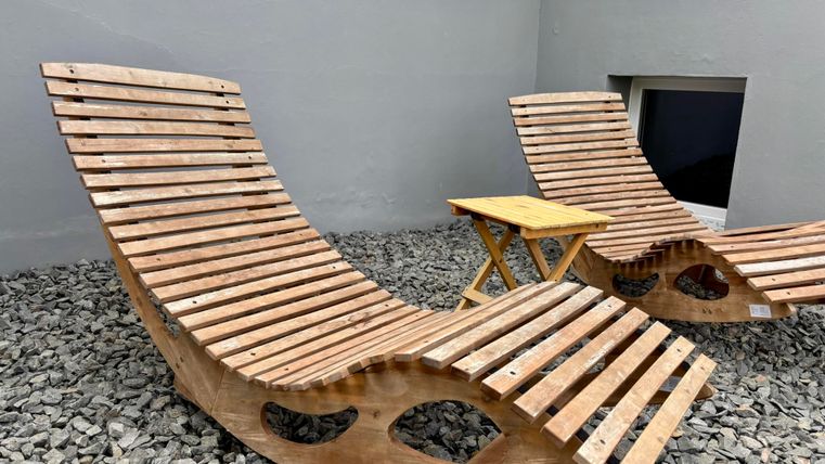 Deux chaises longues en bois confortables sont sur un sol en gravier. Une petite table est placée entre les chaises longues.