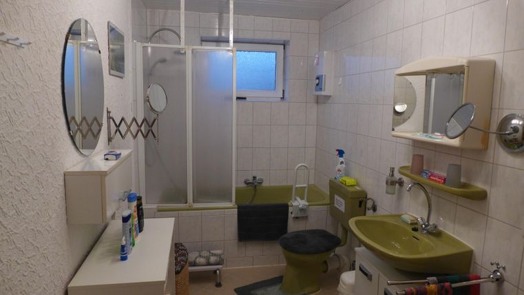 A bathroom with green sanitary fixtures and modern mirrors. The walls are brightly tiled, and there is a shower with a glass partition.