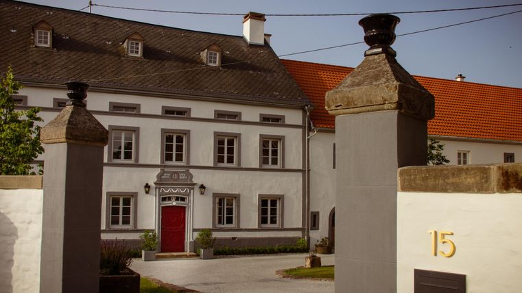 Un bâtiment élégant avec une porte rouge et de grandes fenêtres. Il est entouré d'un mur avec des colonnes et présente une entrée invitante.