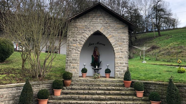 Kleine stenen kapel met een Mariabeeld en planten in potten.