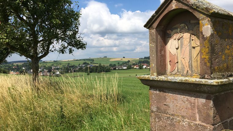 Steinrelief am Wegesrand mit Landschaft im Hintergrund.