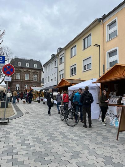 Een drukke straatmarkt met kraampjes en veel mensen. De wolken aan de lucht doen vermoeden dat er mogelijk weersverandering aankomt.