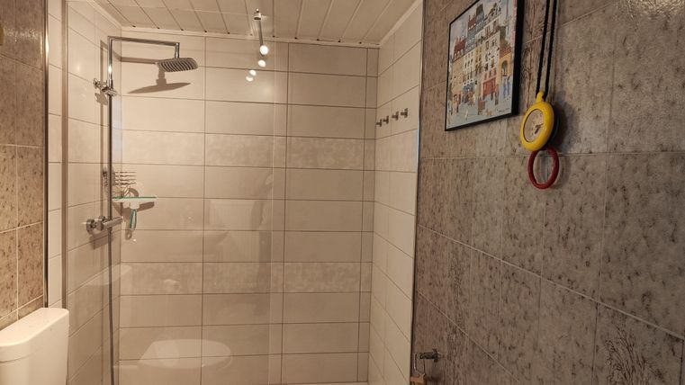 Ein modernes Badezimmer mit einer Dusche, einem WC und gefliesten Wänden. An der Wand hängen Handtücher und ein Bild.